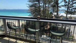 Un balcon avec trois chaises et une bougie, donnant sur une plage et l’océan.