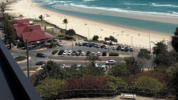 Une vue côtière avec une plage, un espace de stationnement et des bâtiments au premier plan.
