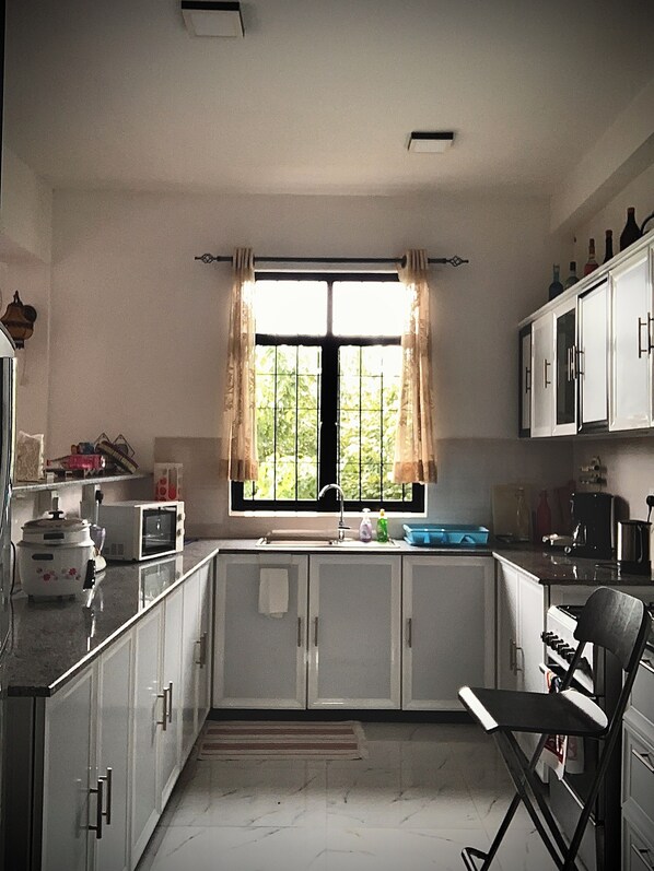 A kitchen with white cabinets, a window with curtains, a sink, and a chair.