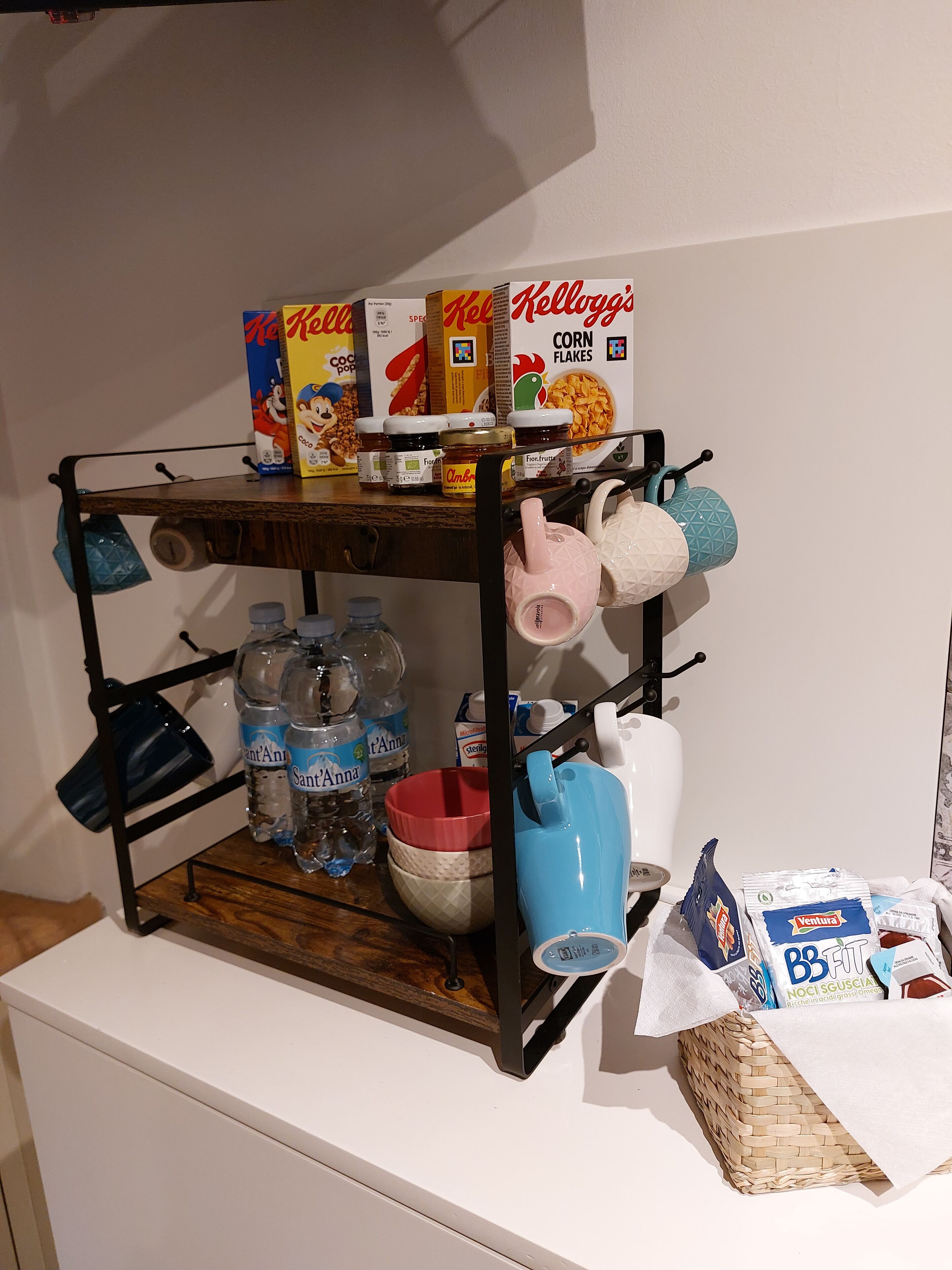 Una encimera de cocina con un estante metálico que contiene varios objetos como frascos, botellas y cajas.