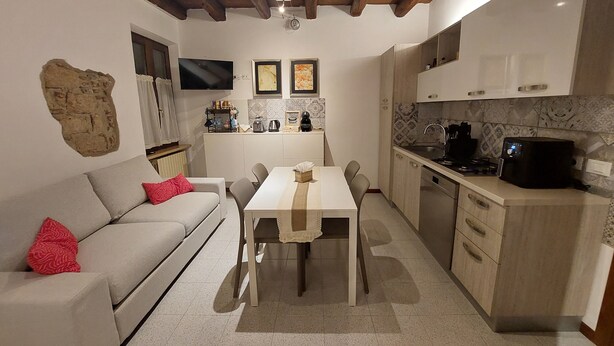 A compact kitchen with a dining table, a sofa with red pillows, and a stone wall feature. - Atelier del Teatro – Charm and Romance in the Heart of Verona (Verona)