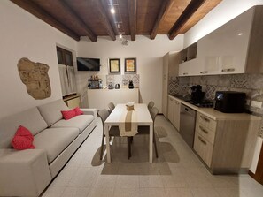 A compact kitchen with a dining table, a sofa with red pillows, and a stone wall feature. - Atelier del Teatro – Charm and Romance in the Heart of Verona (Verona)