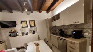 A compact kitchen with a dining area, wooden ceiling beams, a flat-screen TV, and a coffee machine. - Atelier del Teatro – Charm and Romance in the Heart of Verona (Verona)