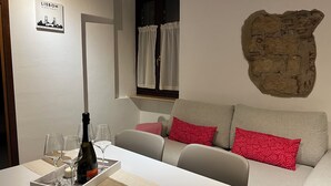 A cozy room with a white sofa, red patterned pillows, a table with wine glasses and a bottle, a wall-mounted sign reading "Lisbon Portugal", and a large stone wall. - Atelier del Teatro – Charm and Romance in the Heart of Verona (Verona)