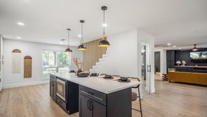 A modern kitchen with a central island, pendant lighting, and a staircase leading to another level. - Western Boots & Spa-Hot Tub, BBQ, Firepit, Gameroom & Good Times! (Houston)