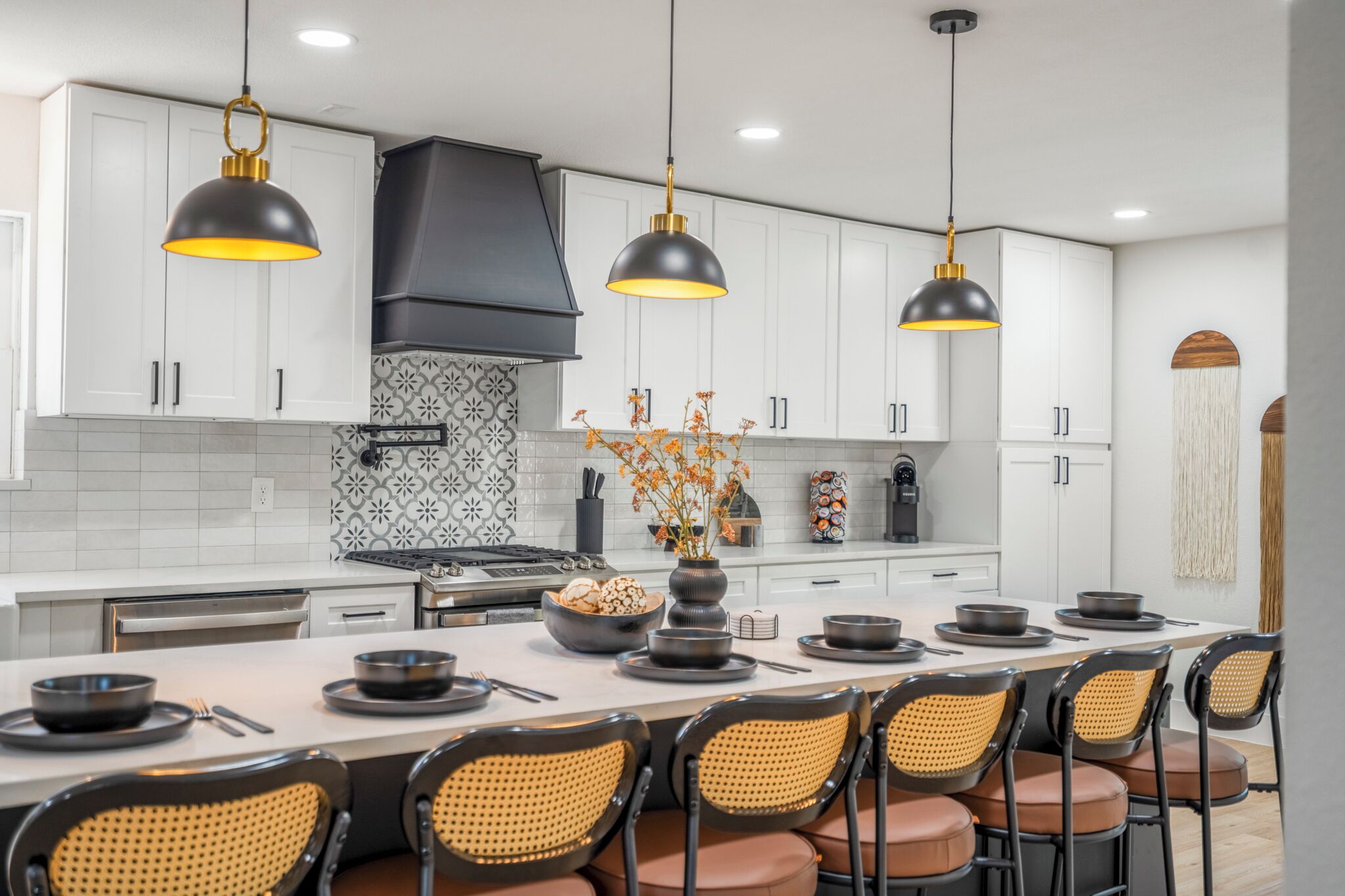 A modern kitchen with white cabinets, black pendant lights, and a central island with seating.