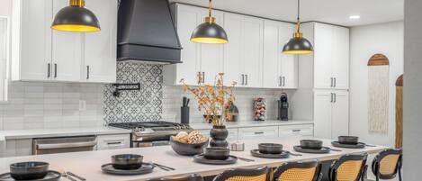 A modern kitchen with white cabinets, black pendant lights, and a central island with seating.