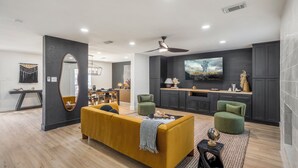 A modern living room with a sofa, two armchairs, a TV, and a kitchen area. - Western Boots & Spa-Hot Tub, BBQ, Firepit, Gameroom & Good Times! (Houston)