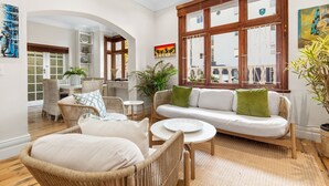 Ein geräumiger Wohnbereich mit Korbmöbeln, einem weißen Sofa und einem großen Fenster mit Holzrahmen.