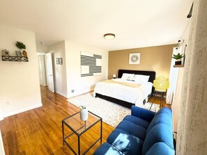 Een slaapkamer met een bed, een blauwe bank, een bijzettafeltje en een bedlampje.