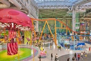 Parque de atracciones cubierto con montañas rusas, una atracción temática de setas y una zona circular central con diseño rosa y verde.