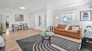 Ein modernes Wohnzimmer mit einer braunen Ledersofa, einem Glastisch und einem grauen Teppich mit Muster.