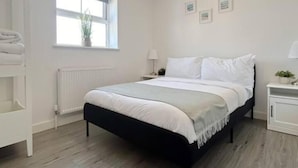 Une chambre à coucher avec un lit, des tables de chevet, une fenêtre et un radiateur.