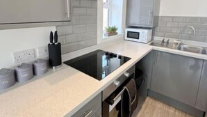 Une cuisine moderne avec des meubles gris, une plaque de cuisson à induction noire, un four à micro-ondes et un évier en acier inoxydable.
