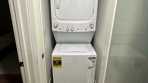 A compact laundry room with a front-loading washer and dryer, a door with a handle, and a wooden floor.