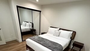 A modern bedroom with a large bed, a fluffy rug, a nightstand, and a mirror.