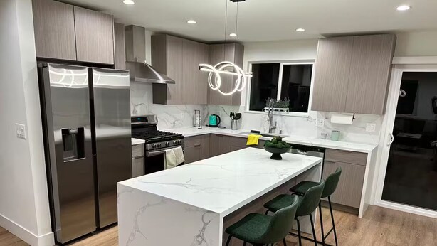 A modern kitchen with a central island, stainless steel appliances, and green bar stools.