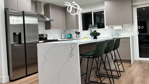 A modern kitchen with a marble island, bar stools, and a stainless steel refrigerator.