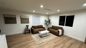 A spacious living room with hardwood flooring, a brown sofa set, a white coffee table, and a potted plant.