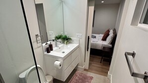A modern bathroom with a toilet, sink, and mirror. There is a small rug on the floor and a plant on the sink.