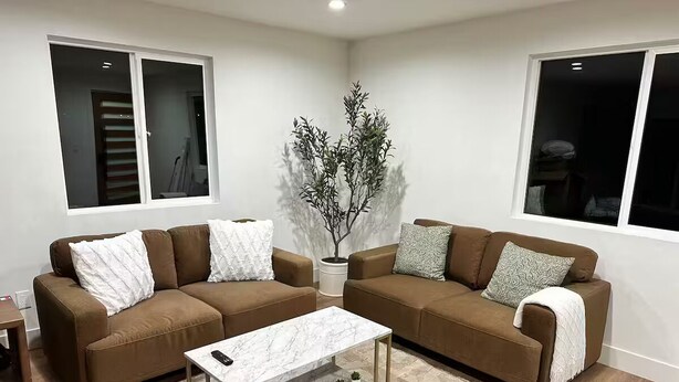 A living room with two brown sofas, a white marble coffee table, and a small potted plant.