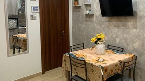 A dining area with a table set for four, a wall-mounted TV, and a mirror reflecting a kitchen area. - Girasole Marino - Beautiful apartment near the sea and the center of Palermo (Palermo)