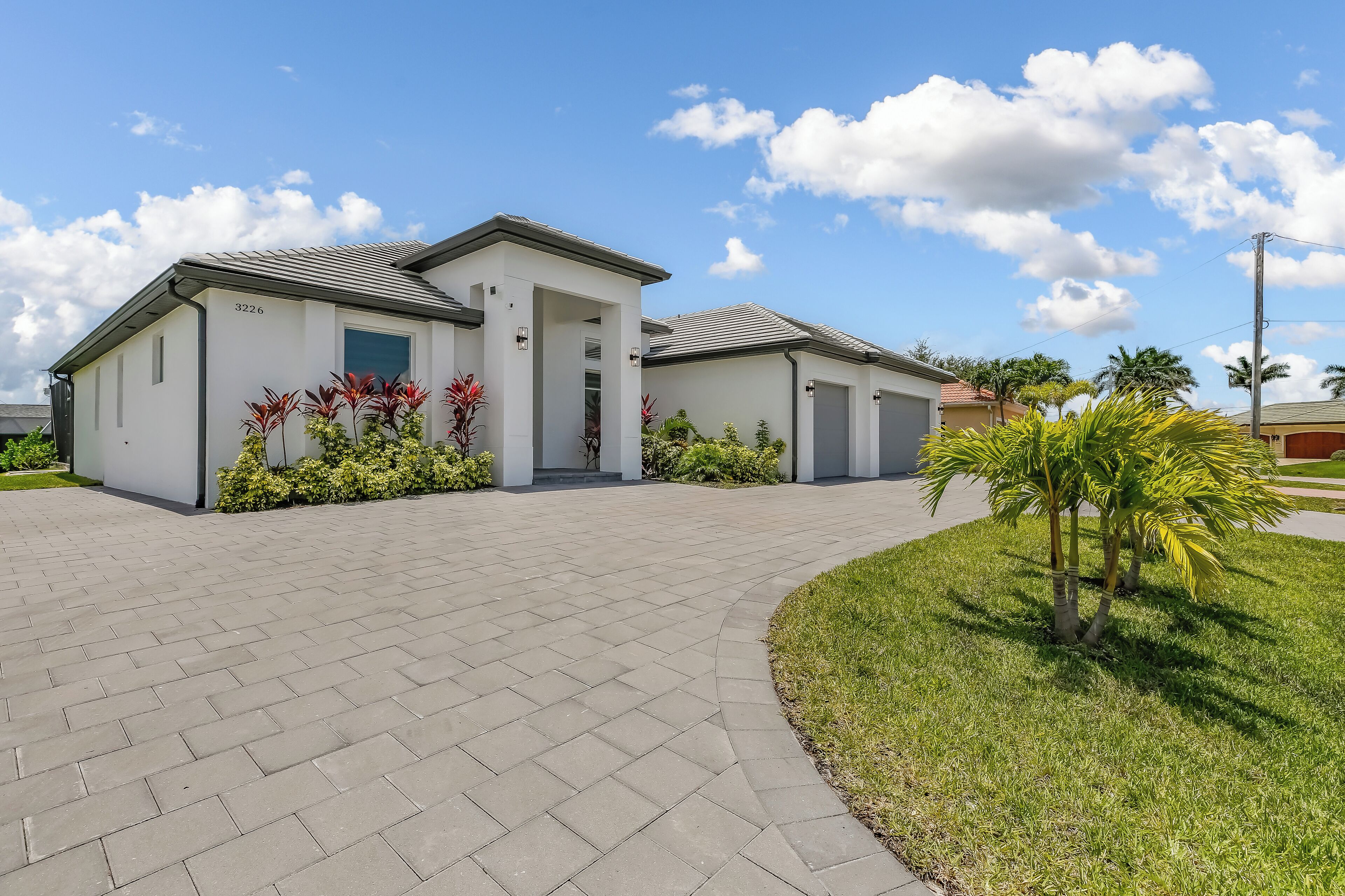 A modern residential building with a paved driveway, a covered entrance, and a well-maintained lawn with small trees.