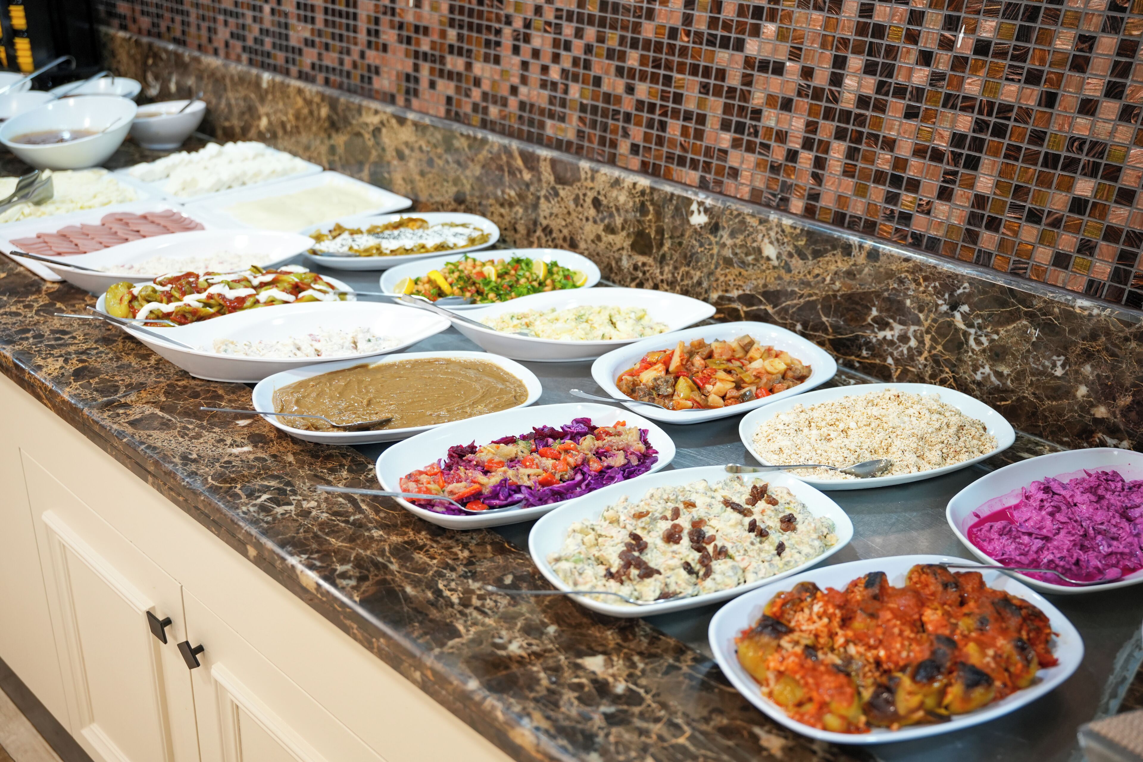 A buffet with various dishes arranged on a marble countertop.