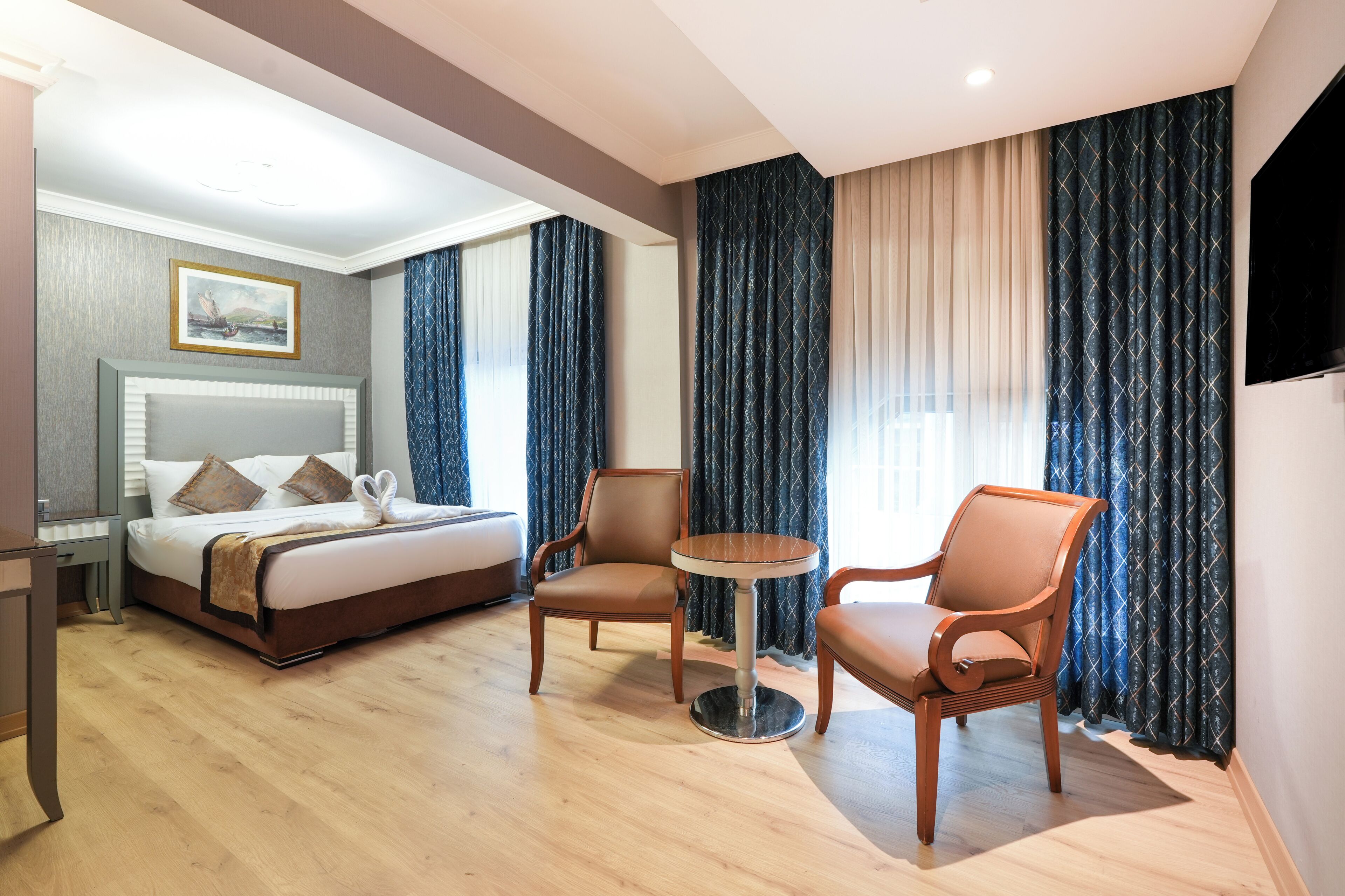 A hotel room with a bed, two chairs, a small table, a TV, and curtains.