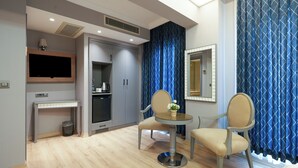 A hotel room with a TV mounted on the wall, a small table with chairs, a kitchenette, and a large window with blue curtains. - Taksim Stare Hotel (Istanbul)