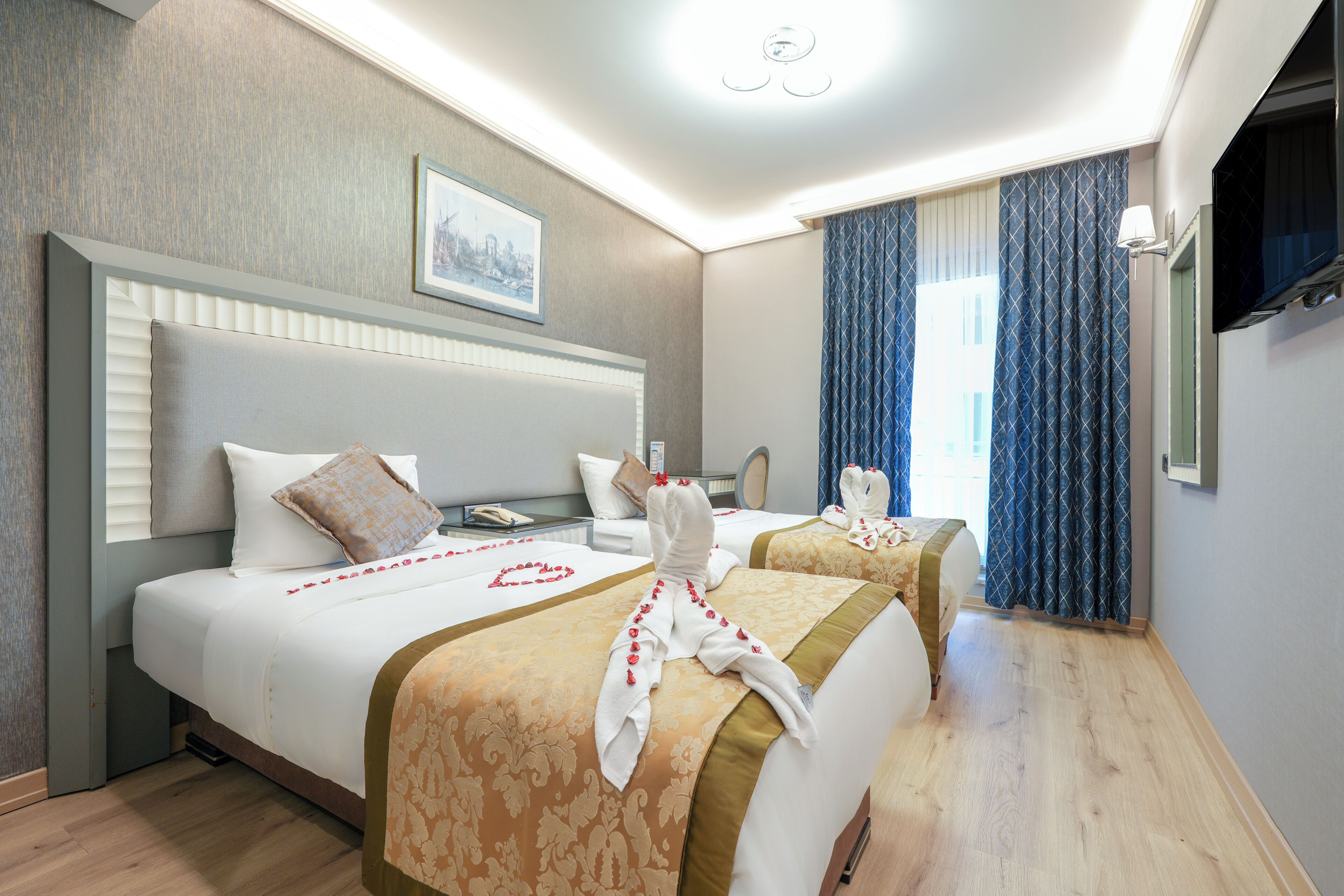 A hotel room with two beds, a flat-screen TV, a framed picture on the wall, and a window with curtains.