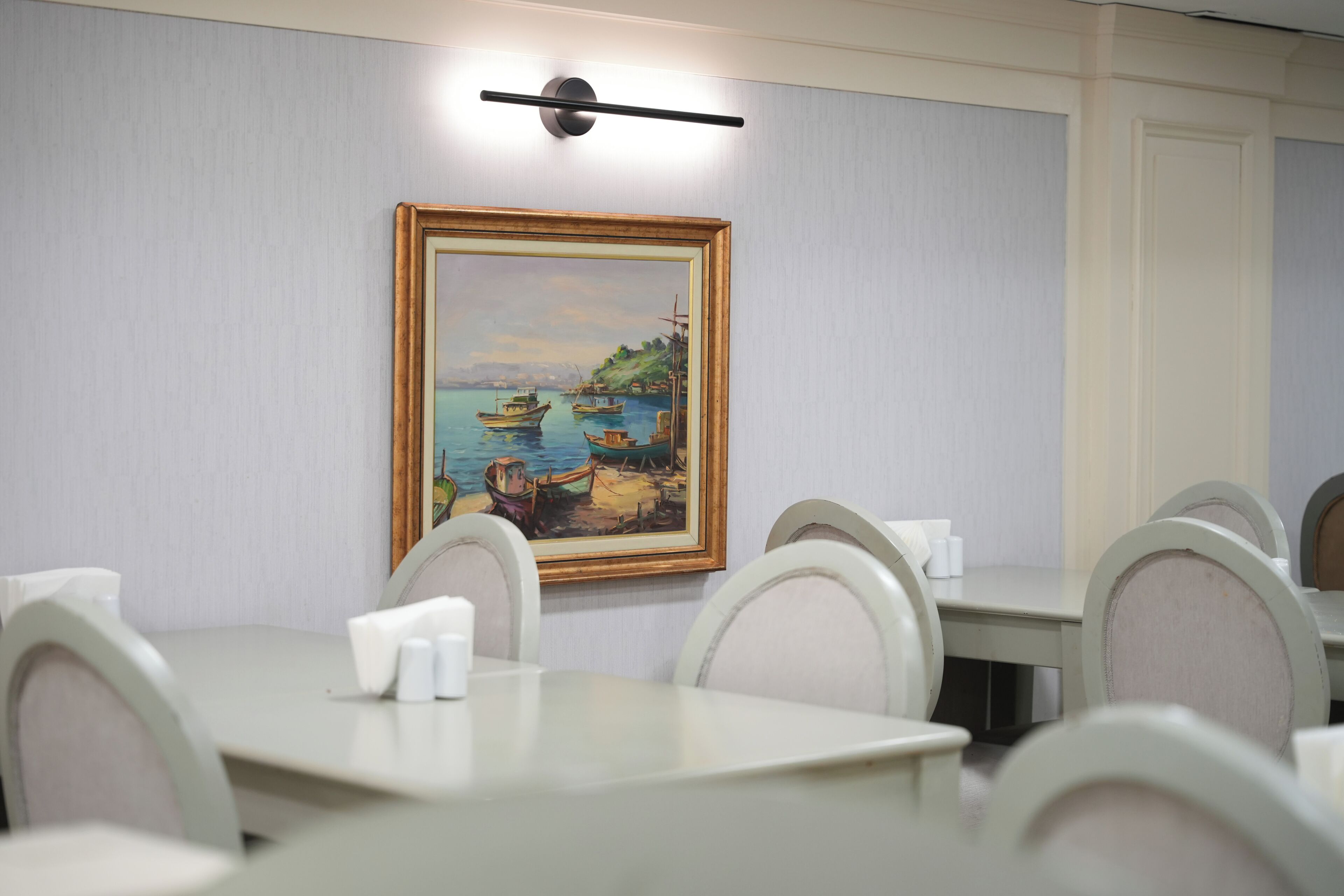 A conference room with a painting of a coastal scene, white tables, and chairs.