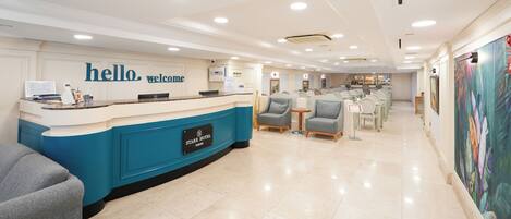 A hotel reception area with a blue counter, a 'hello welcome' sign, and a reception desk.