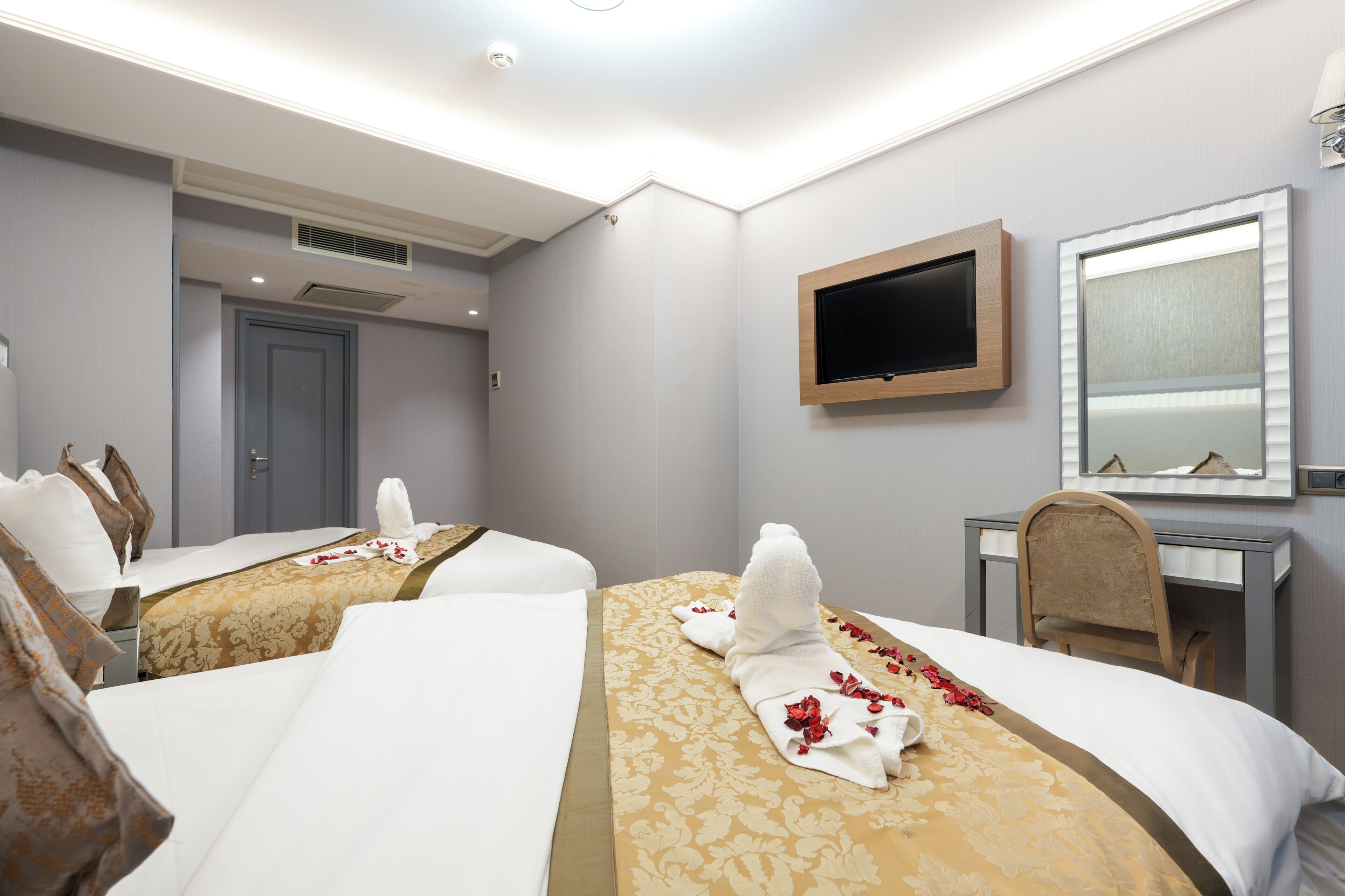 A hotel room with two beds, a TV, a desk, and a mirror.