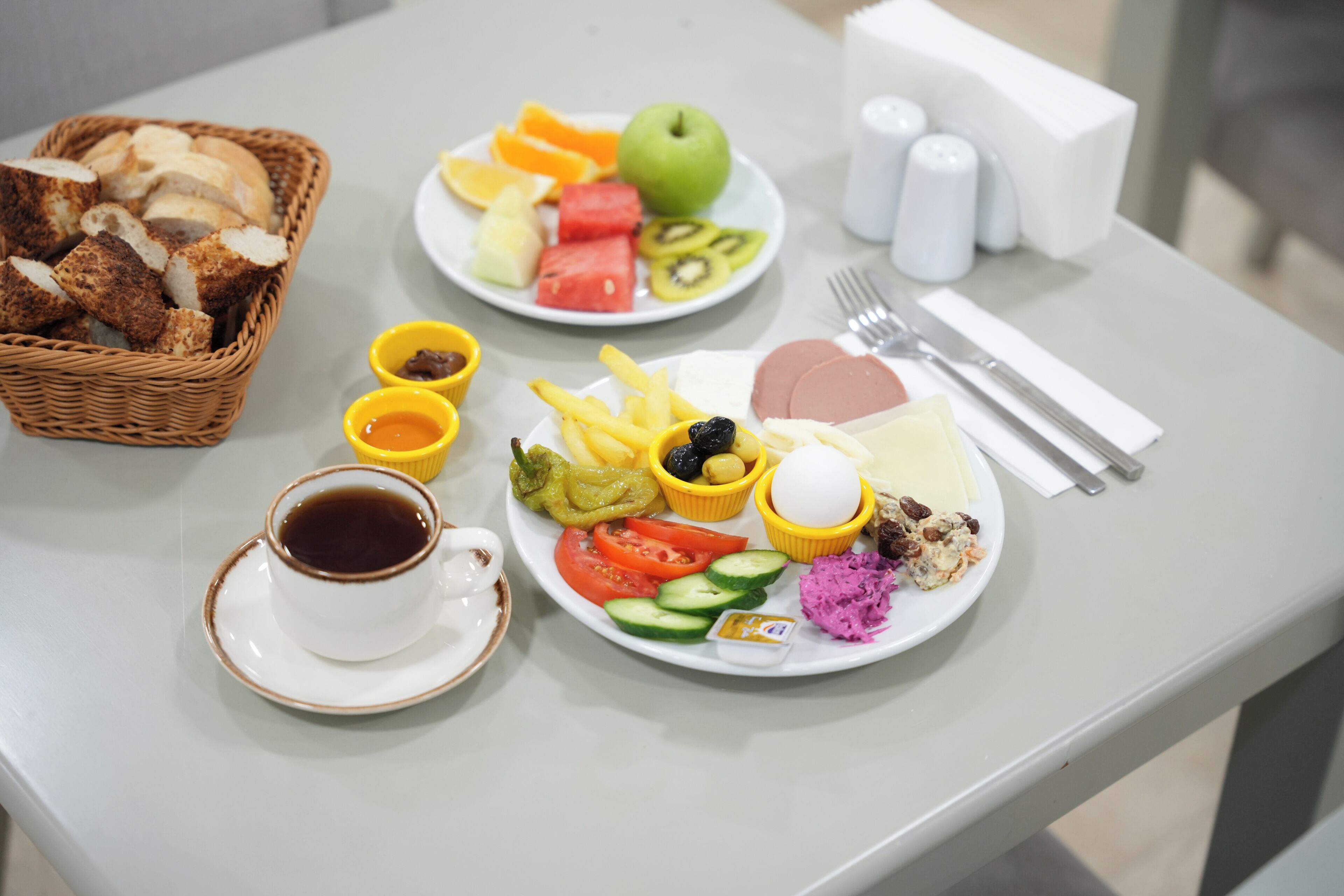 Un desayuno con pan, fruta, huevos y café sobre una mesa.