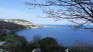 Un pueblo costero con vistas despejadas al mar, un pequeño puerto deportivo y una colina con edificaciones.