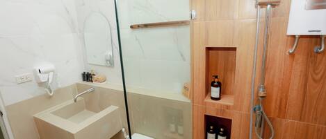 A bathroom with a glass shower enclosure, a sink, and wooden shelves with toiletries.