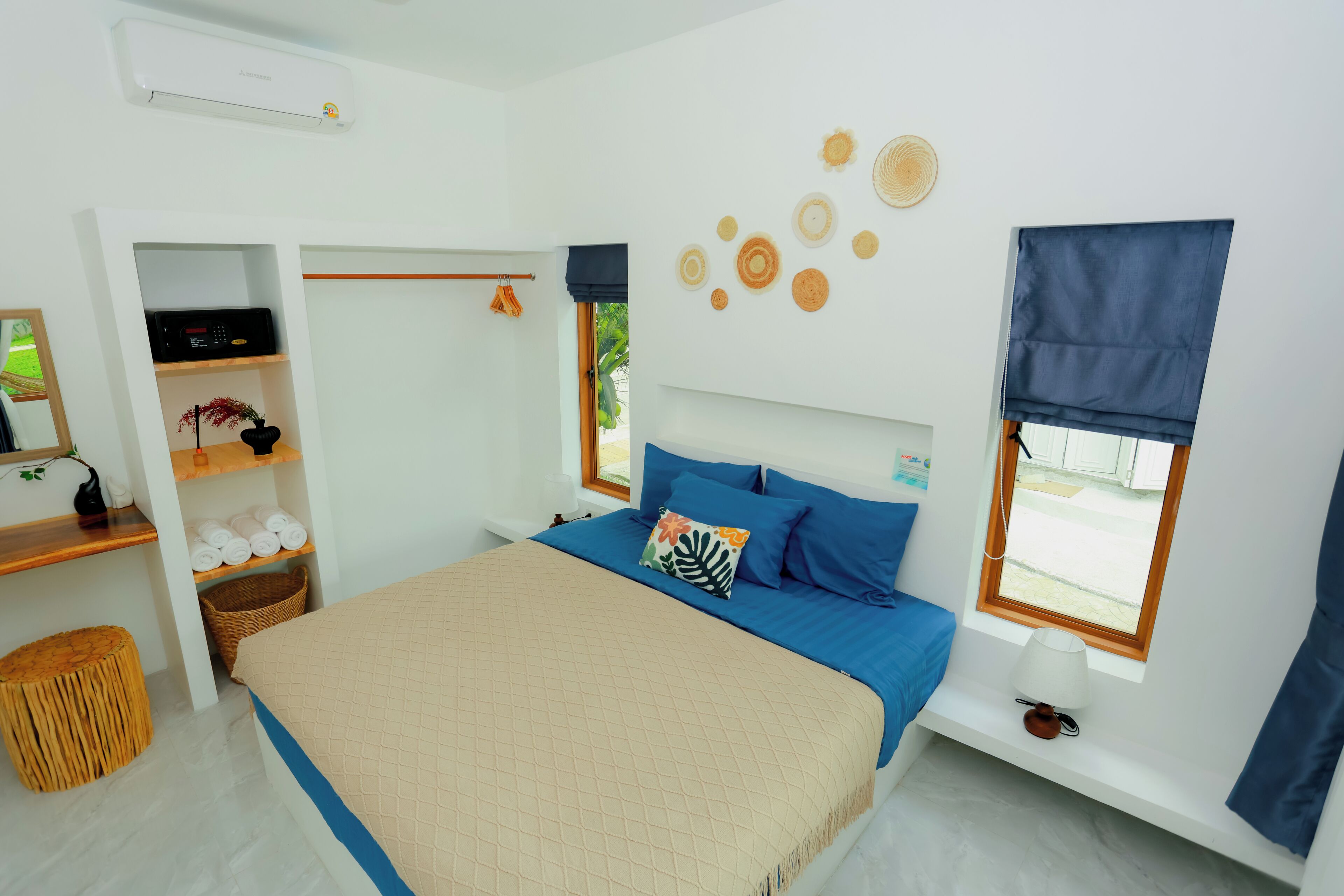 Een slaapkamer met een bed, een kledingkast, een plank met handdoeken, een mand, een raam met gordijnen en decoraties aan de muur.