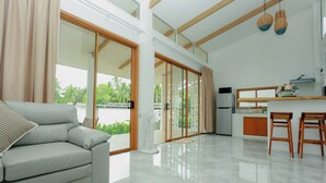 Una sala moderna con sofá, un comedor con sillas, una cocina con refrigerador y puertas de vidrio grandes que dan a un balcón.