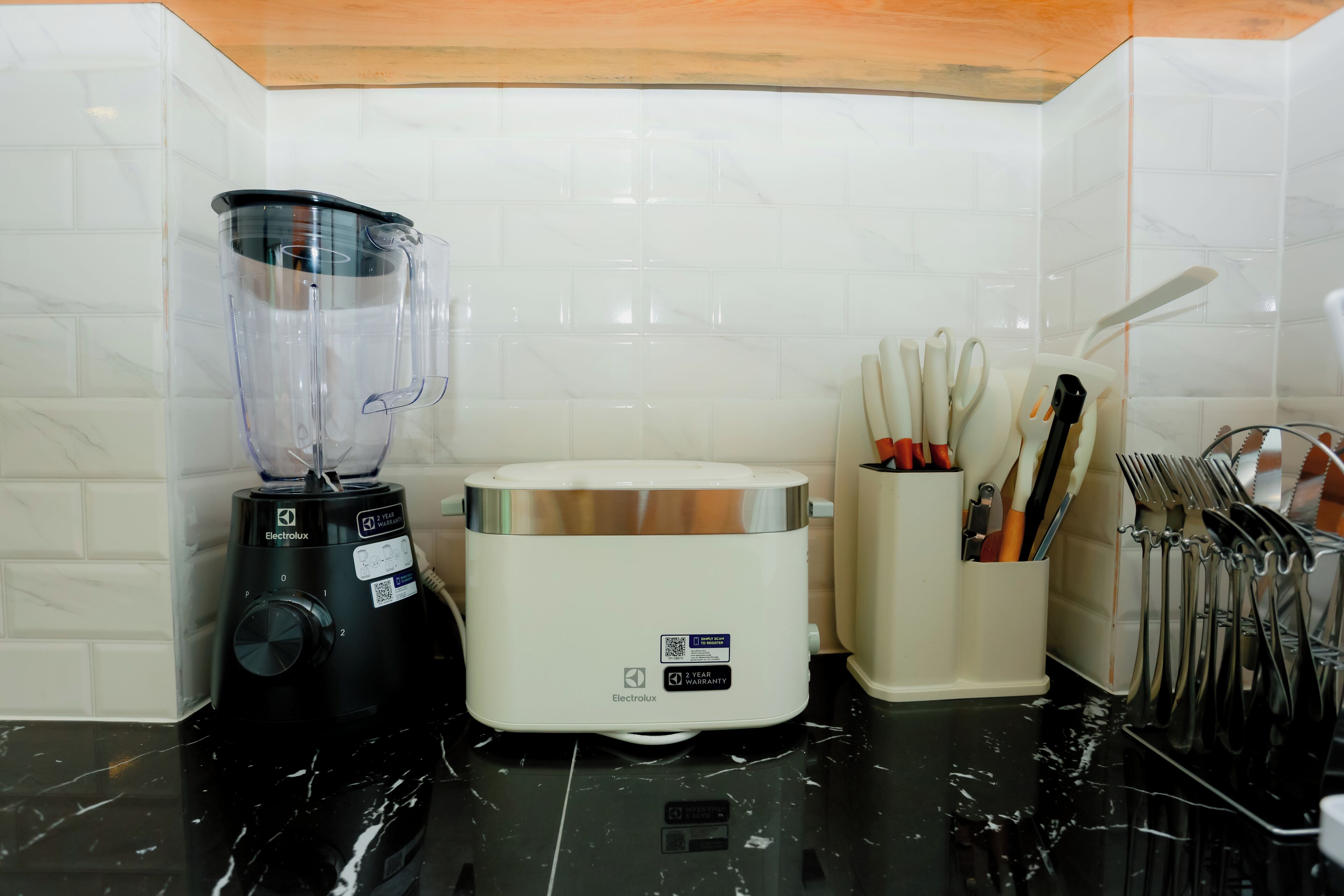 A kitchen with a blender, toaster, and utensil holder on a black countertop.