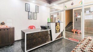 A reception area with a reception desk, framed pictures on the wall, a ceiling fan, and a staircase leading to an upper floor. - PP Palace (Puri)