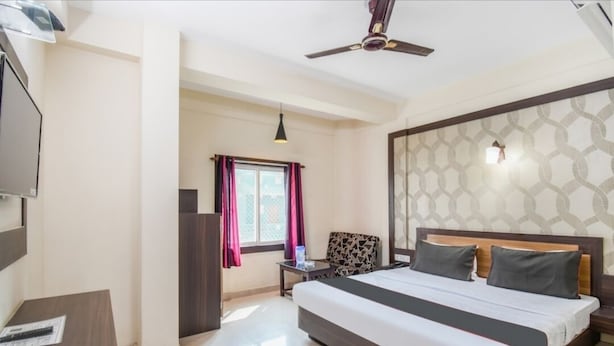 A hotel room with a large bed, a ceiling fan, a TV, a small table, and a window with curtains. - PP Palace (Puri)
