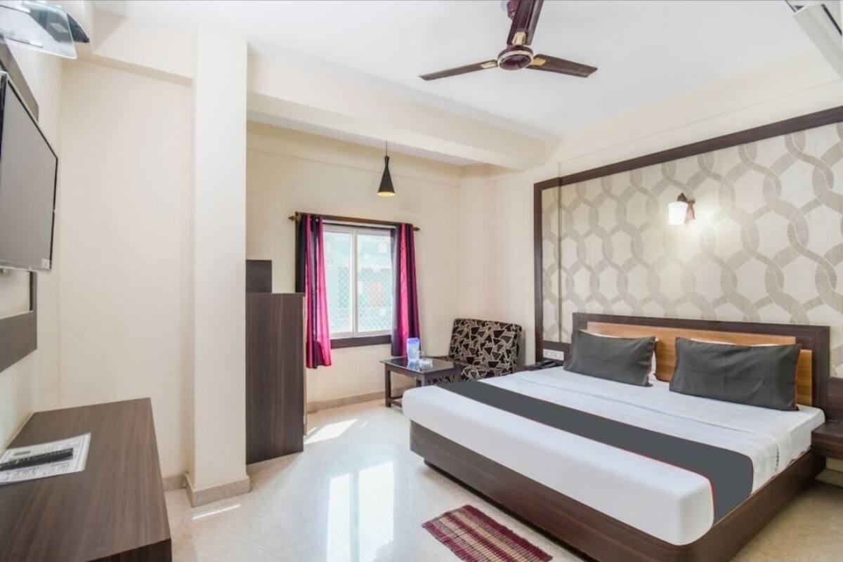 A hotel room with a large bed, a ceiling fan, a TV, a small table, and a window with curtains.
