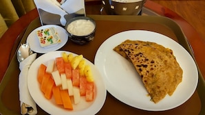 Een dienblad met een bord met gesneden fruit, een bakje yoghurt en een gevouwen platbrood.