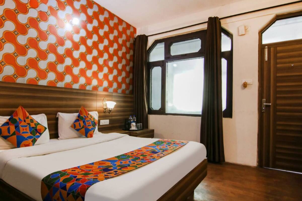 Hotelkamer met een groot bed, nachtkastje, wandlamp, raam met gordijnen en een deur.