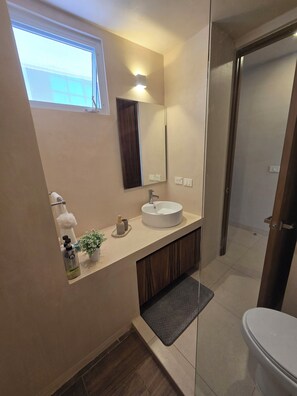 A modern bathroom with a large mirror, a sink, and a toilet. There is a window providing natural light and a small plant on the countertop. - Peaceful Jungle Studio in Reverence, Tulum   (Tulum)