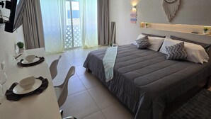 Quarto de hotel com uma cama, uma escrivaninha com cadeira, um ventilador de teto e um apanhador de sonhos na parede.