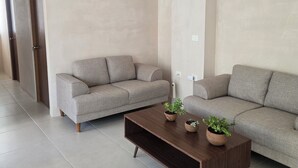 Uma sala de estar moderna com dois sofás cinzas, uma mesa de centro de madeira com plantas em vasos e piso ladrilhado.