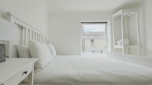 Une pièce blanche avec un lit, un bureau et une fenêtre.