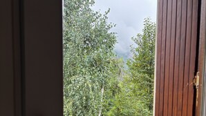 Une vue à travers une fenêtre avec une porte en bois, qui révèle une rivière, de la verdure et une personne au loin.
